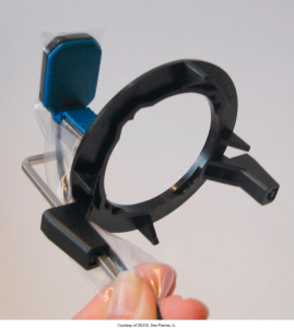 A hand holding an anterior beam alignment device used in dental radiography, featuring a blue sensor cover and a black alignment ring, provided by DEXIS, Des Plaines, IL.