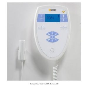 A digital control panel for a dental X-ray machine, with a display showing settings and timer, attached to a wall with a coiled cable, from Sirona Dental Inc., USA, Charlotte, NC.