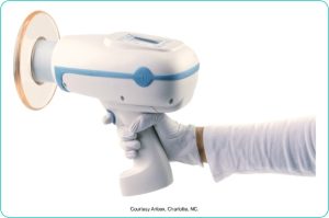 A person wearing gloves holding a portable, handheld dental X-ray device, courtesy of Aribex, Charlotte, NC.