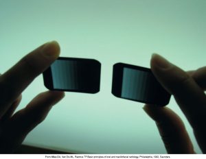 A pair of hands holding two small rectangular radiographic stepwedge density scales against a light source.