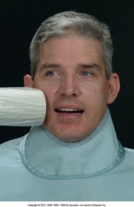 Close-up photo of a male patient with a dental X-ray machine positioned near his mouth for a radiographic examination.