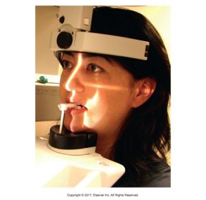 A woman positioned for a dental X-ray procedure, using a bite block and wearing a head-mounted device designed to stabilize her head during the imaging process. The setup ensures precise alignment for accurate diagnostic results.