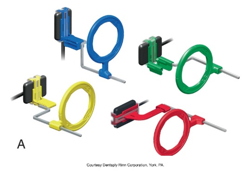 The image shows a collection of various colored dental beam alignment devices, each consisting of a film holder and aiming ring, used to position and align dental X-ray films accurately.