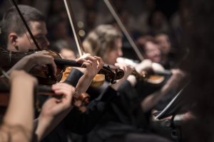 Decorative image of people sitting in a row playing violins.