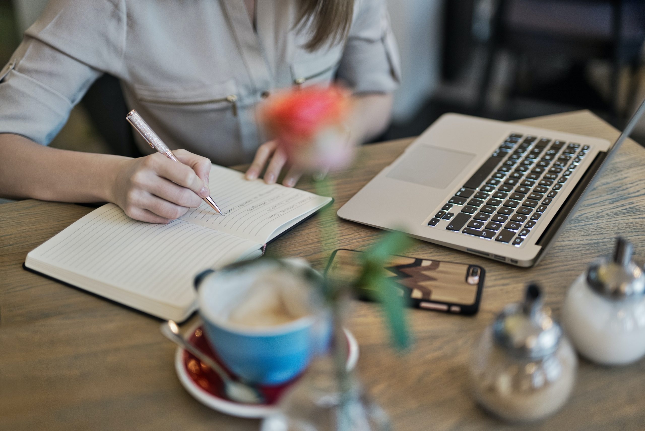 Decorative photograph of a person taking notes via pen and paper at a desk.