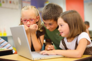 Three children gathered around a laptop.