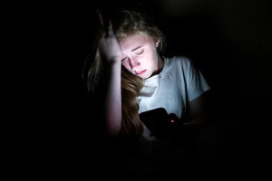 A sad young woman caught in the glow of a laptop.