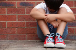 Young boy sitting dejectedly against a brickwall.