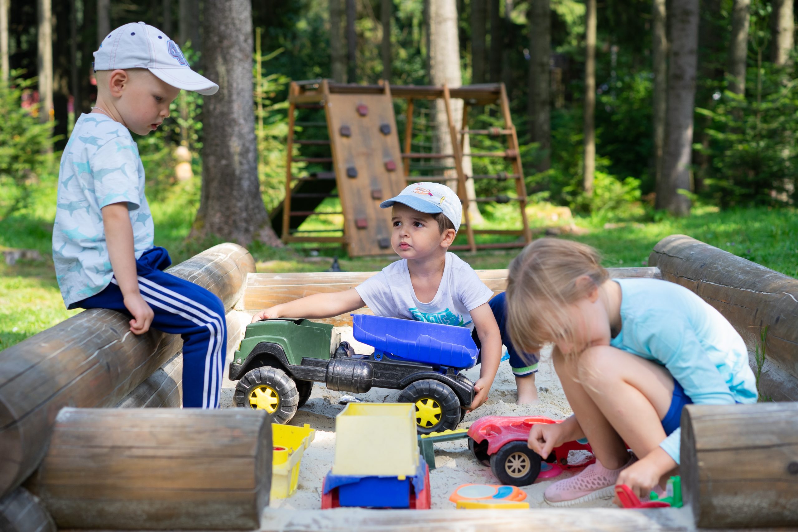 three preschool aged children playing with trucks in an outdoor sandbox