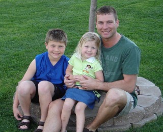 a father and two children sitting on the ground outside