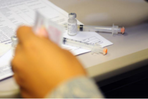 Picture of a hand with vaccine vials sitting on the desk in the background.