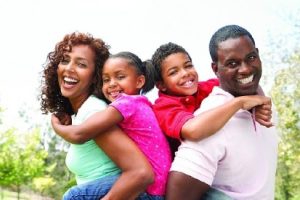 Two smiling parents (male & female) each holding a holding a child on their back.