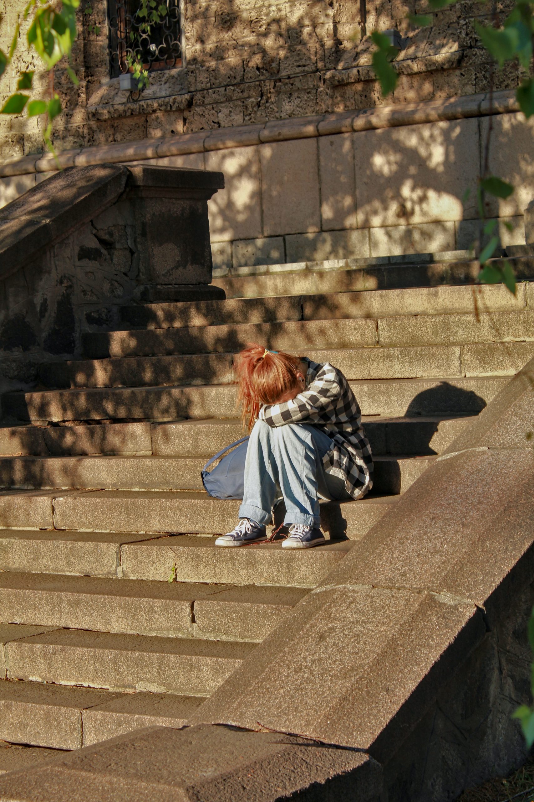 a child sitting alone on a set of stone stairs, resting her head on her knees