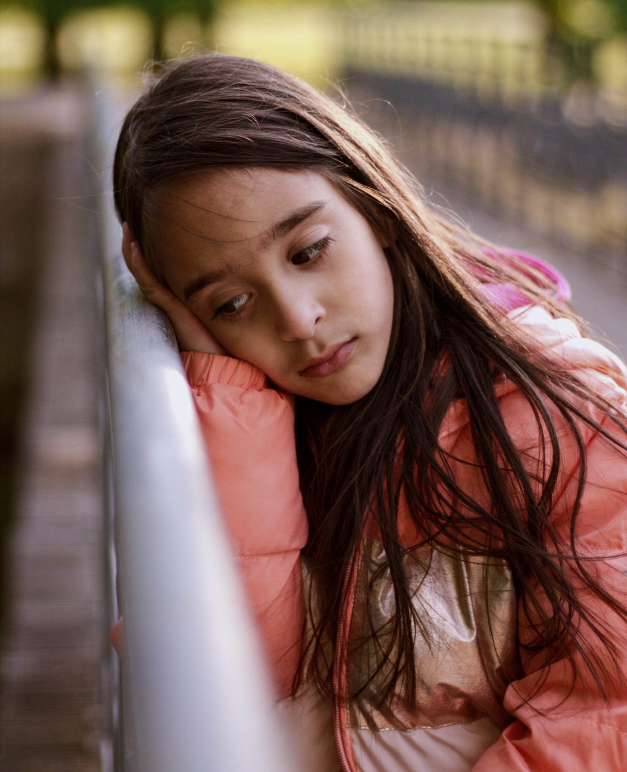 a girl learning up against a chain link fence, resting her head on her hand