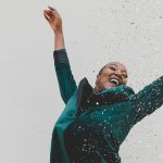 woman in green jacket raising her hands