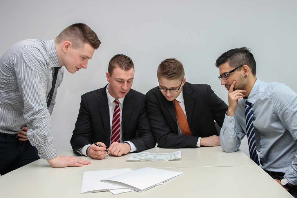 four men in suits looking at pages on a table