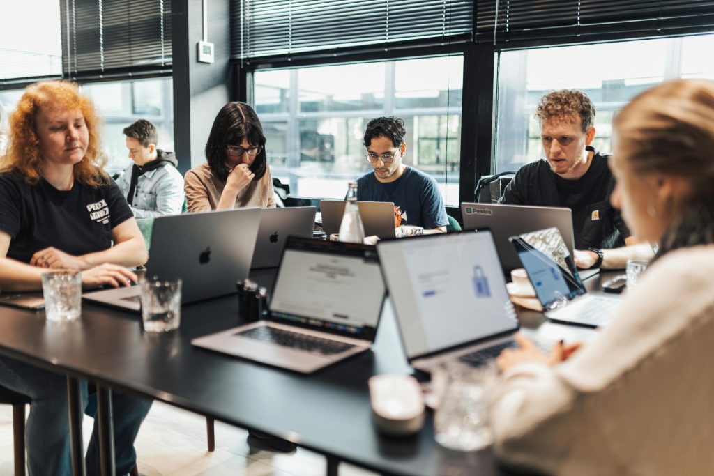 A group of employees are seated at a table together and working on laptops.