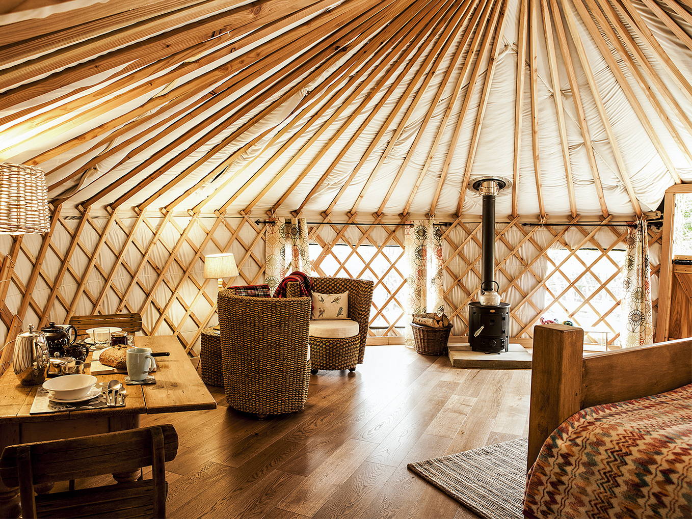 Interior of a luxury yurt, with a bed, table, chairs, and wood stove.