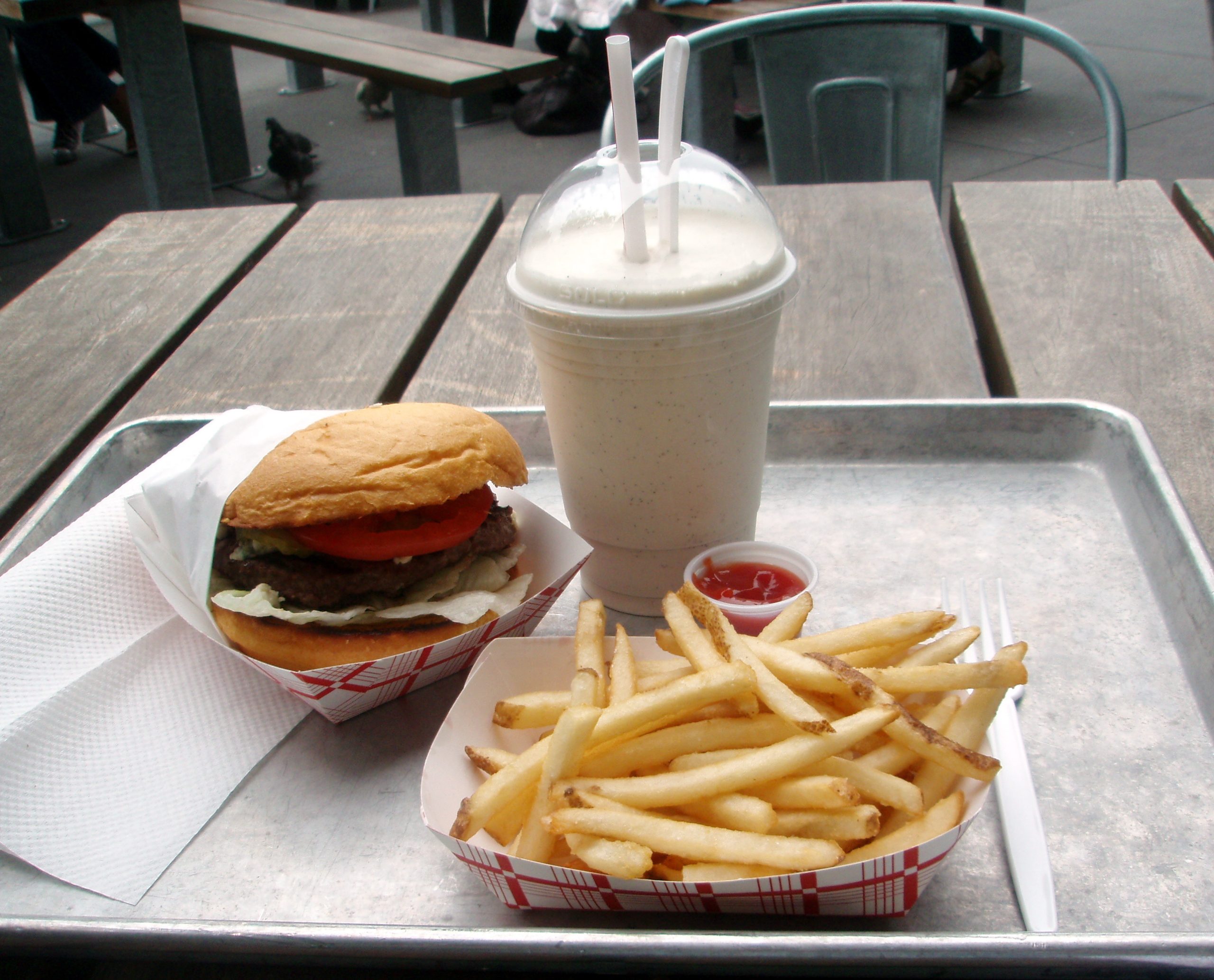 A tray with a burger, milkshake, and french fries with ketchup.