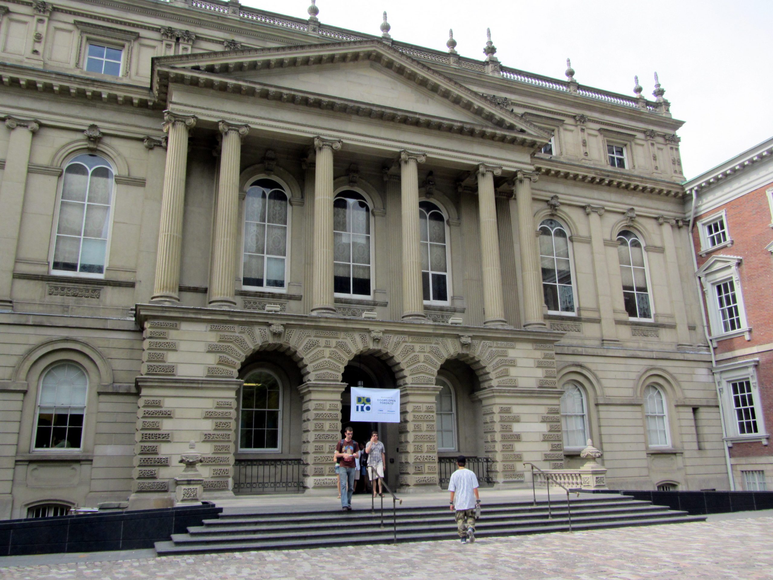 People walking past a Doors Open Toronto event sign posted at the entrance of Osgoode Hall.