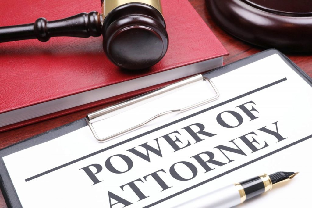 A book with a judge's gavel, the base for the gavel, and a clipboard with document titled Power of Attorney, and a fountain pen.