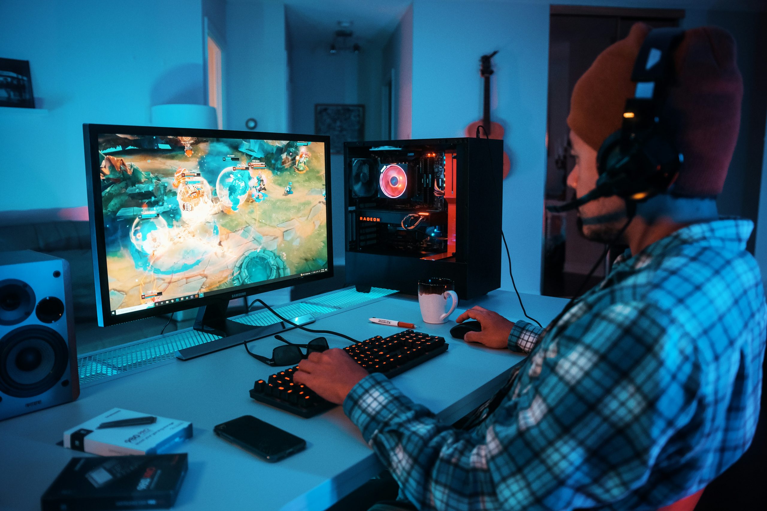Image of a person wearing headphones and playing computer games at a computer desk.