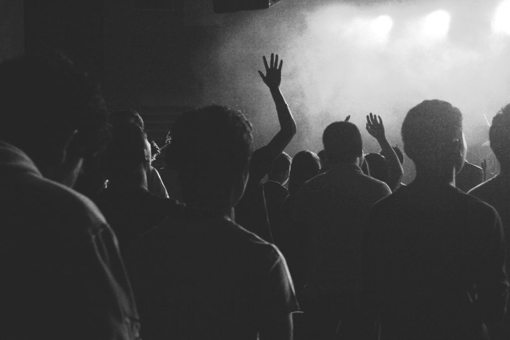 Black and white image of a crowd of people from behind who look like they are observing a performance.