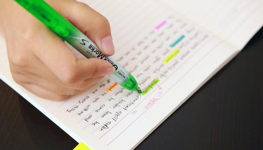 A person's hand using a highlighter to highlight text written in a notebook.