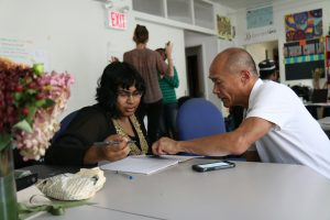 A man sitting at a table helping a colleague with work.