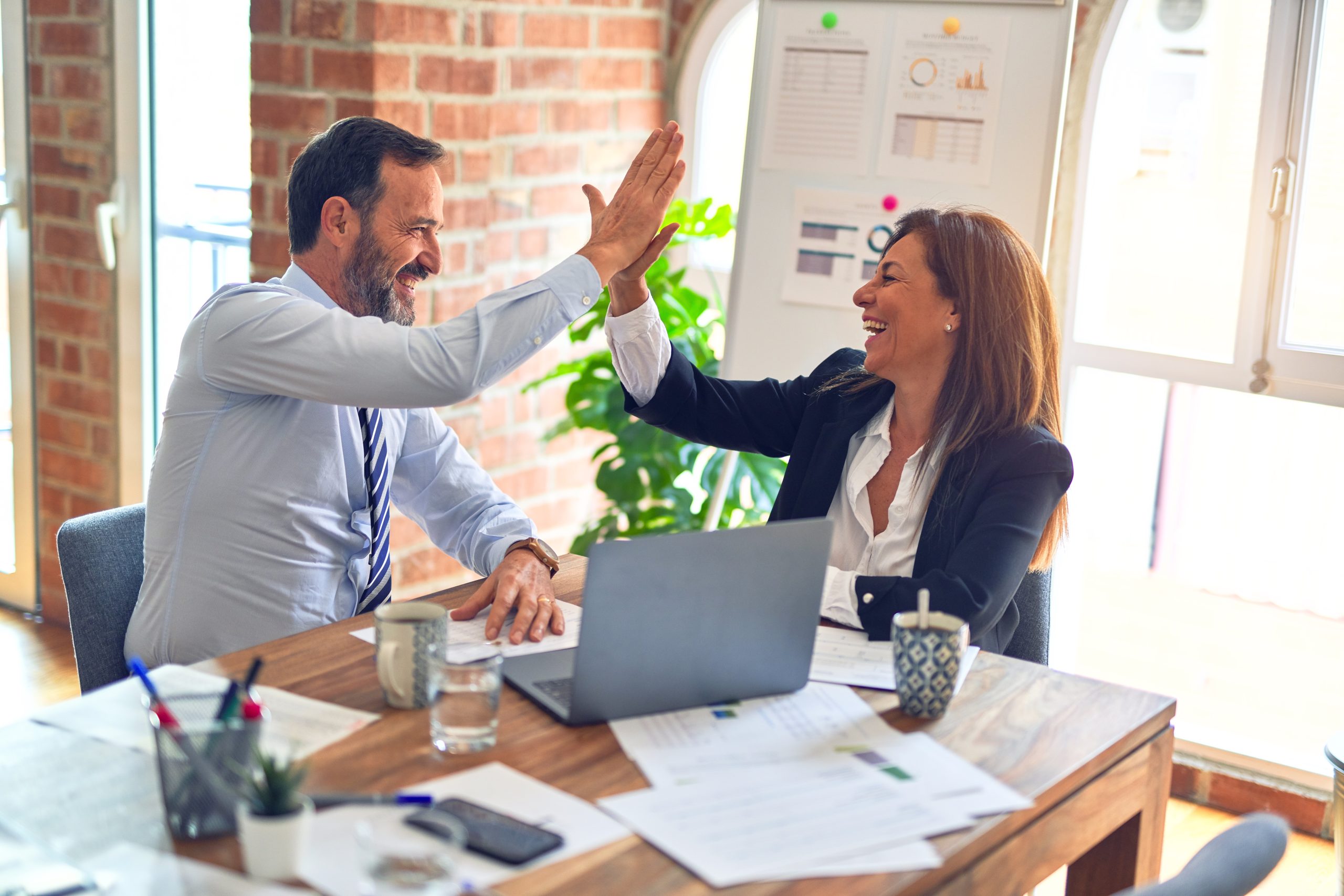 Photo of two middle age business workers smiling happy and confident. Working together with smile on face hand giving high five at the office