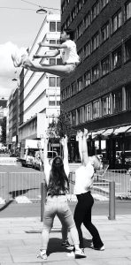 Photo of 3 people who have thrown another person up into the air and are now preparing to follow through by catching the person.