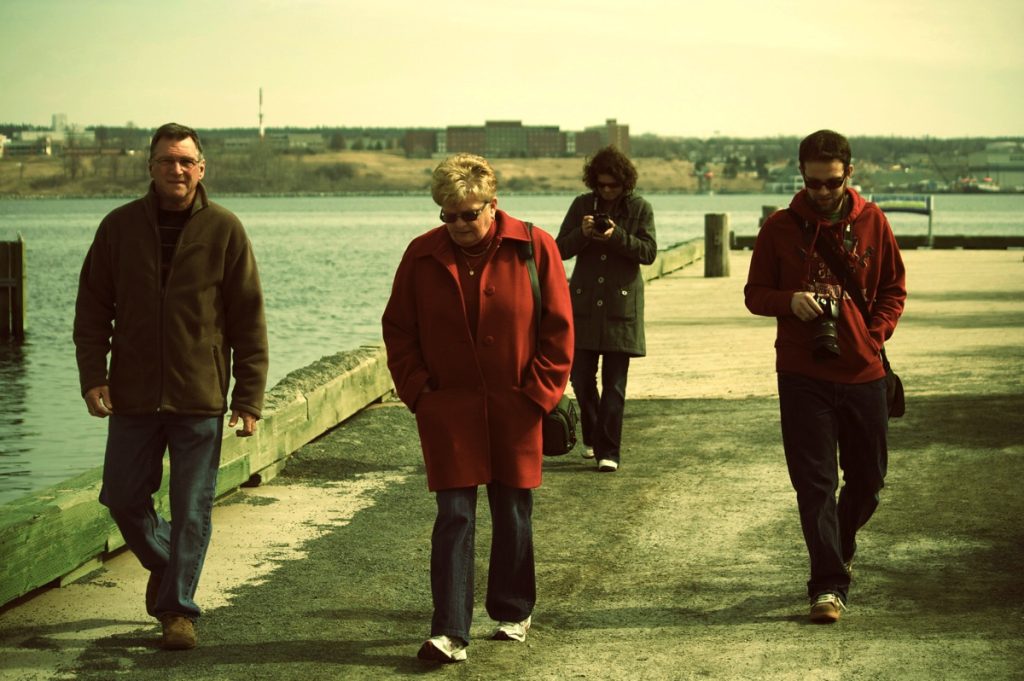 Photo of four people walking near a reservoir. Two are holding cameras.