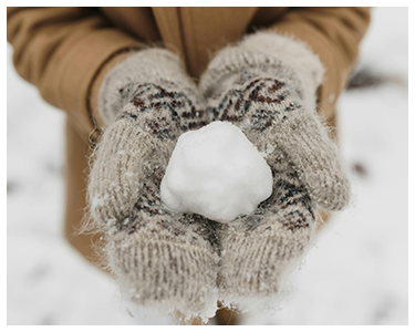 A person wearing thick, wool gloves with a snowball in their hands.