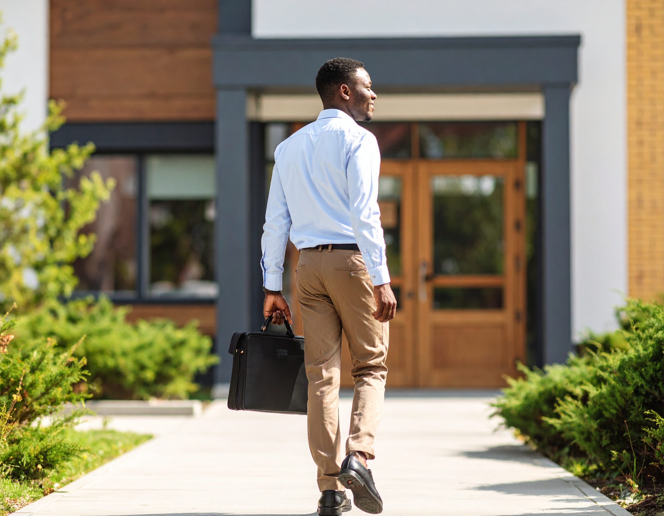 A young male teacher walking toward the entrance of a school with a briefcase in hand.