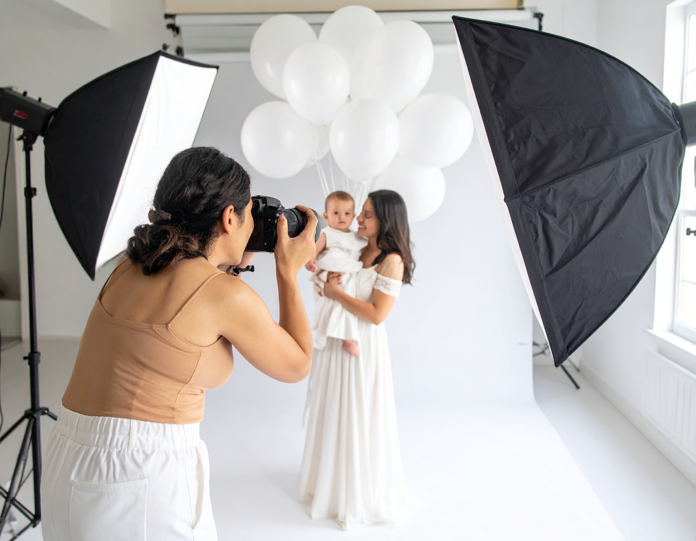 A female photographer taking a photo of a mother and baby at a photoshoot with balloons and professional lighting.