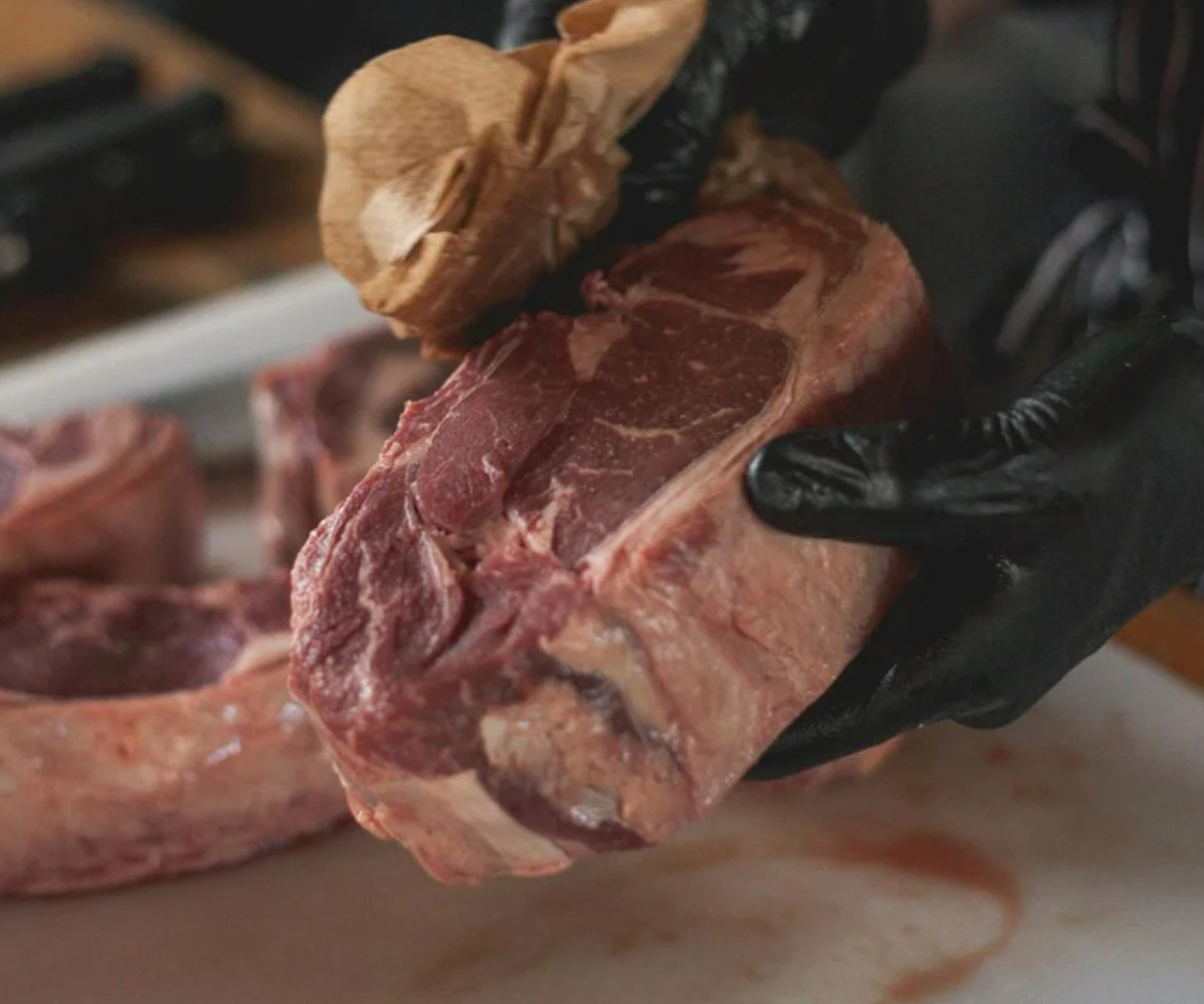 A person wearing gloves cutting meat.