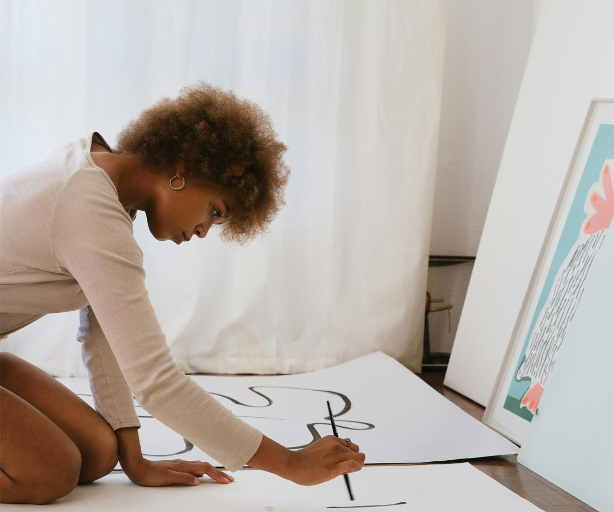 A woman sitting on the floor, painting with a paintbrush.
