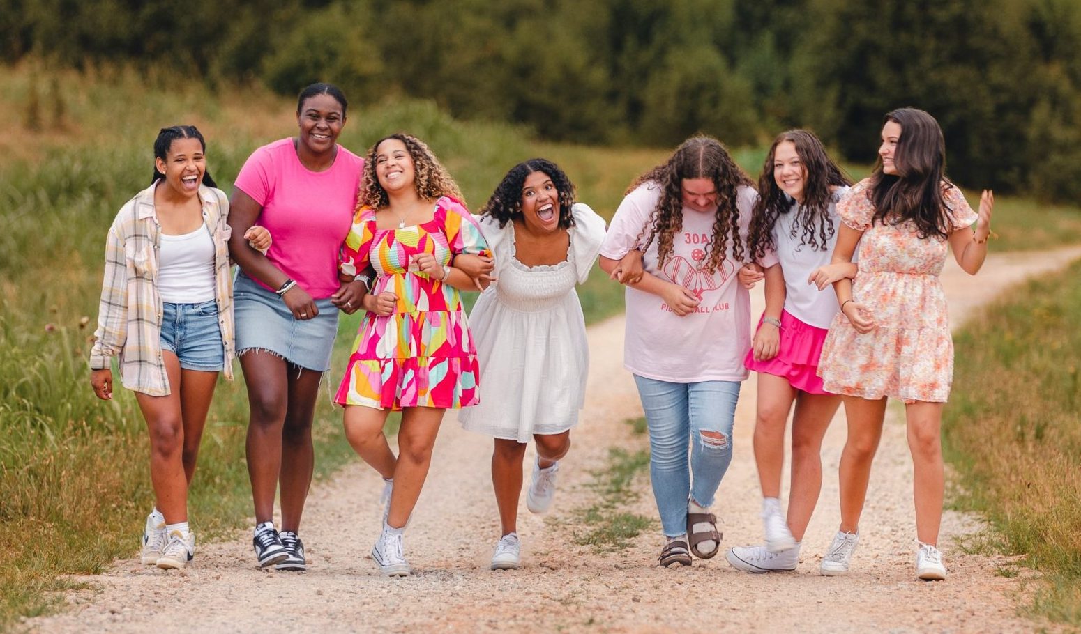 A group of friends wearing summer dresses, t-shirts, and shorts, walking down a trail.