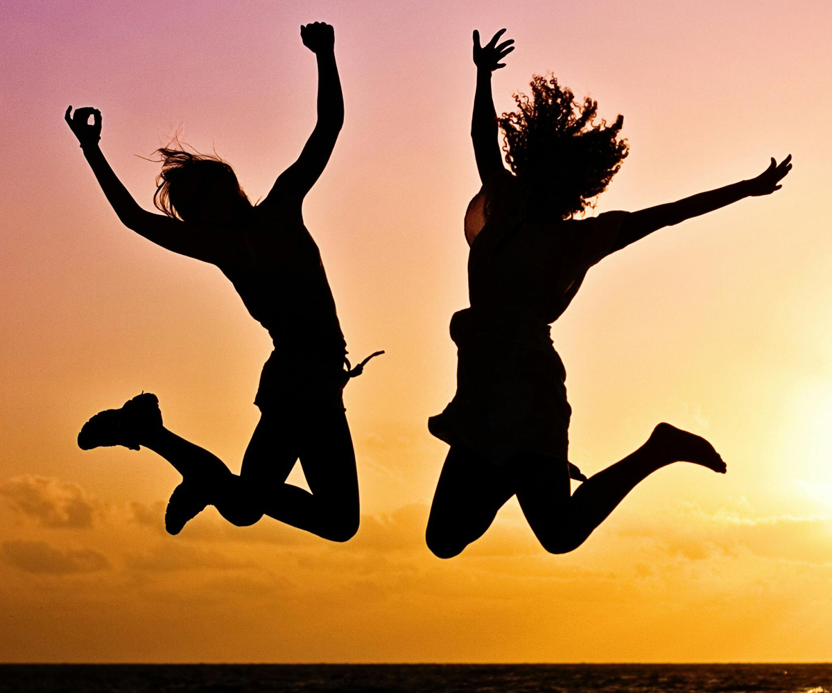 Silhouettes of two people jumping in the air in front of a sunset.