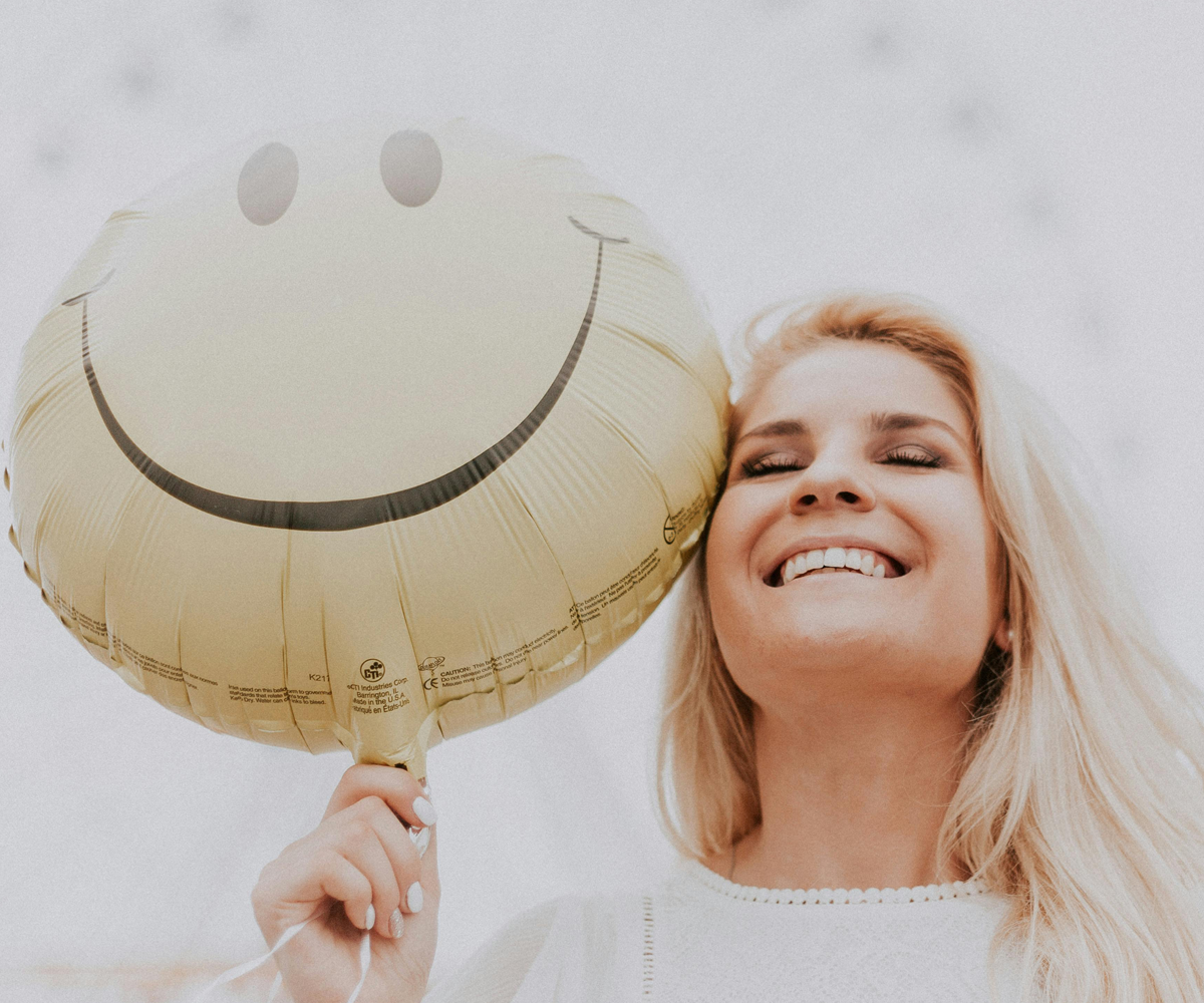 A smiling woman holding a happy face balloon.
