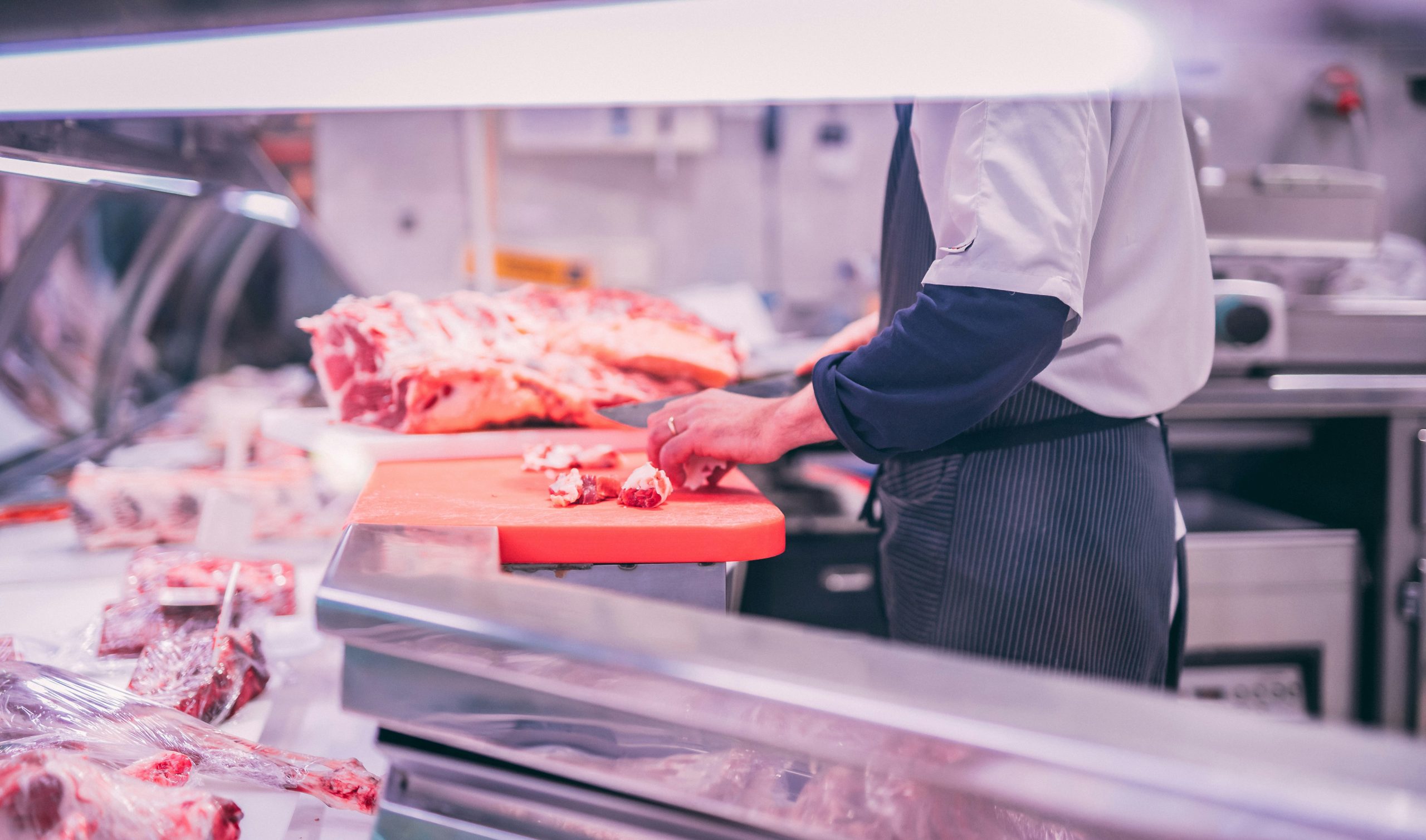 Man behind a butcher shop counter, slicing raw meat.