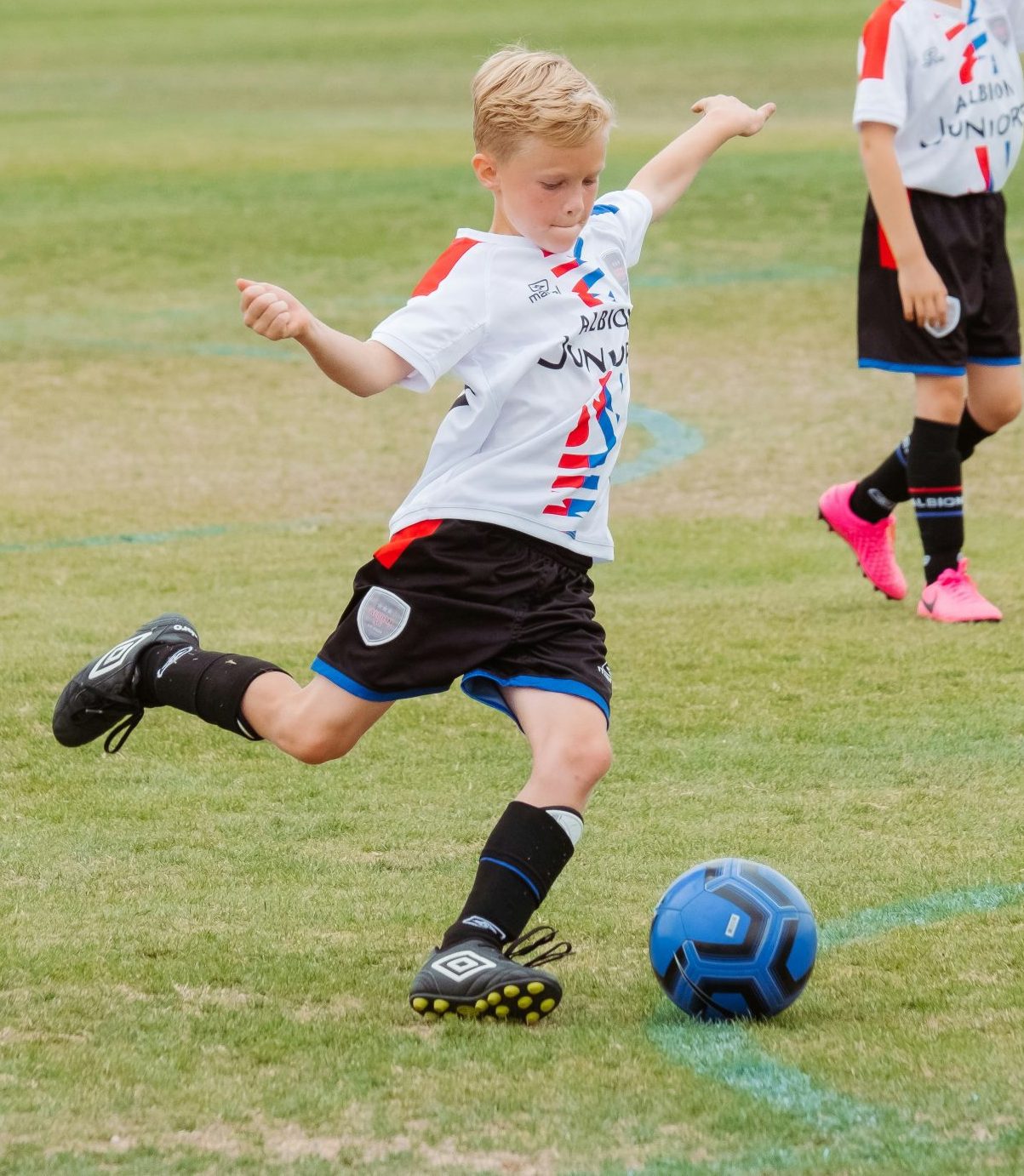 A young boy kicking a soccer ball on a soccer field.