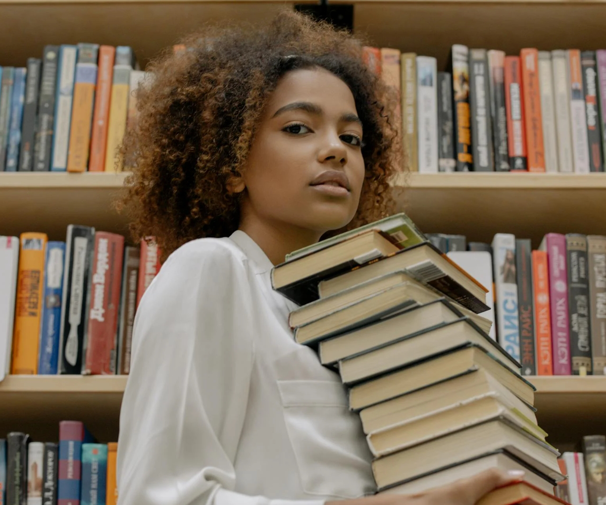 A woman holding a stack of books in a library.