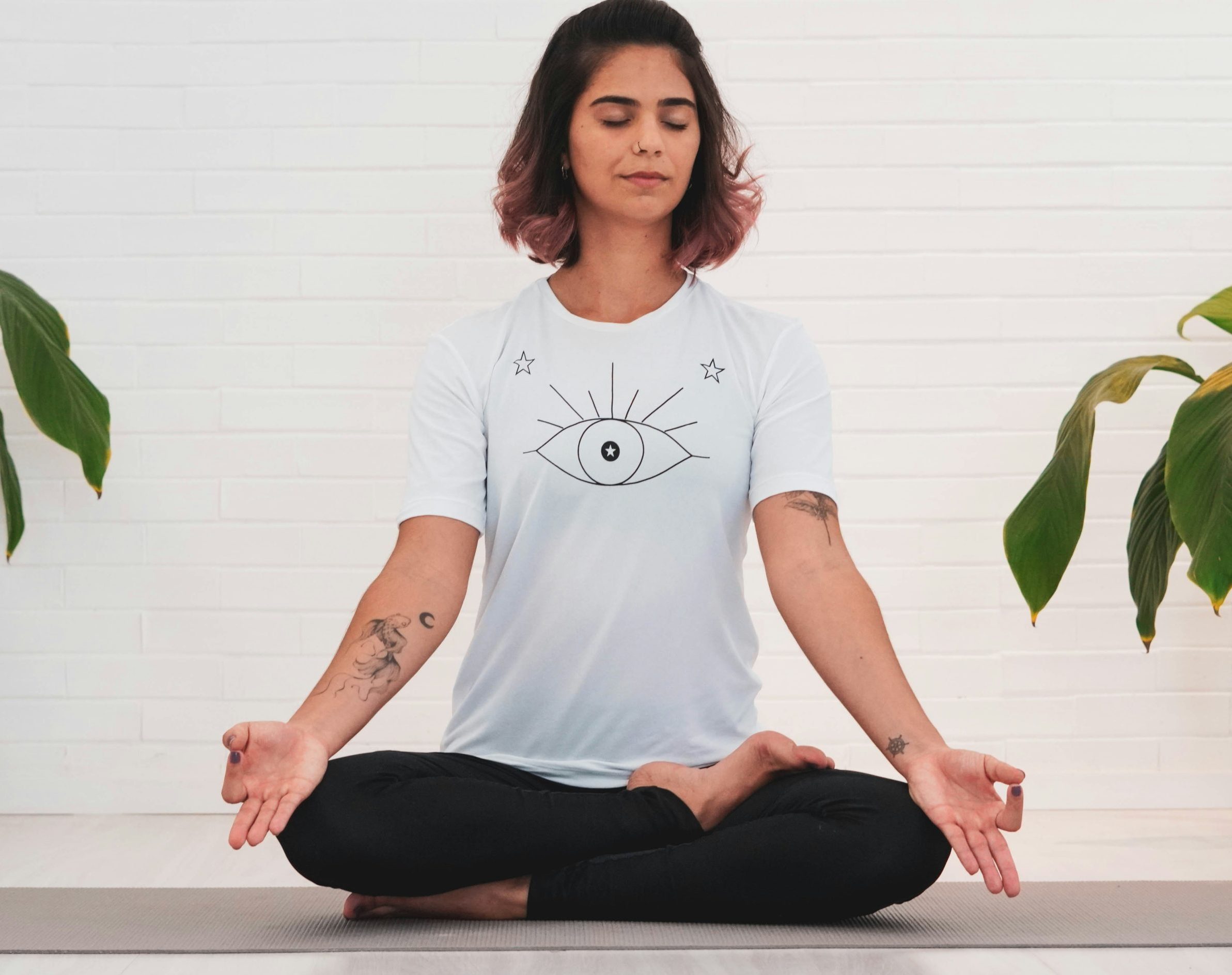 A young woman with eyes closed in a meditative yoga pose, sitting with legs crossed.