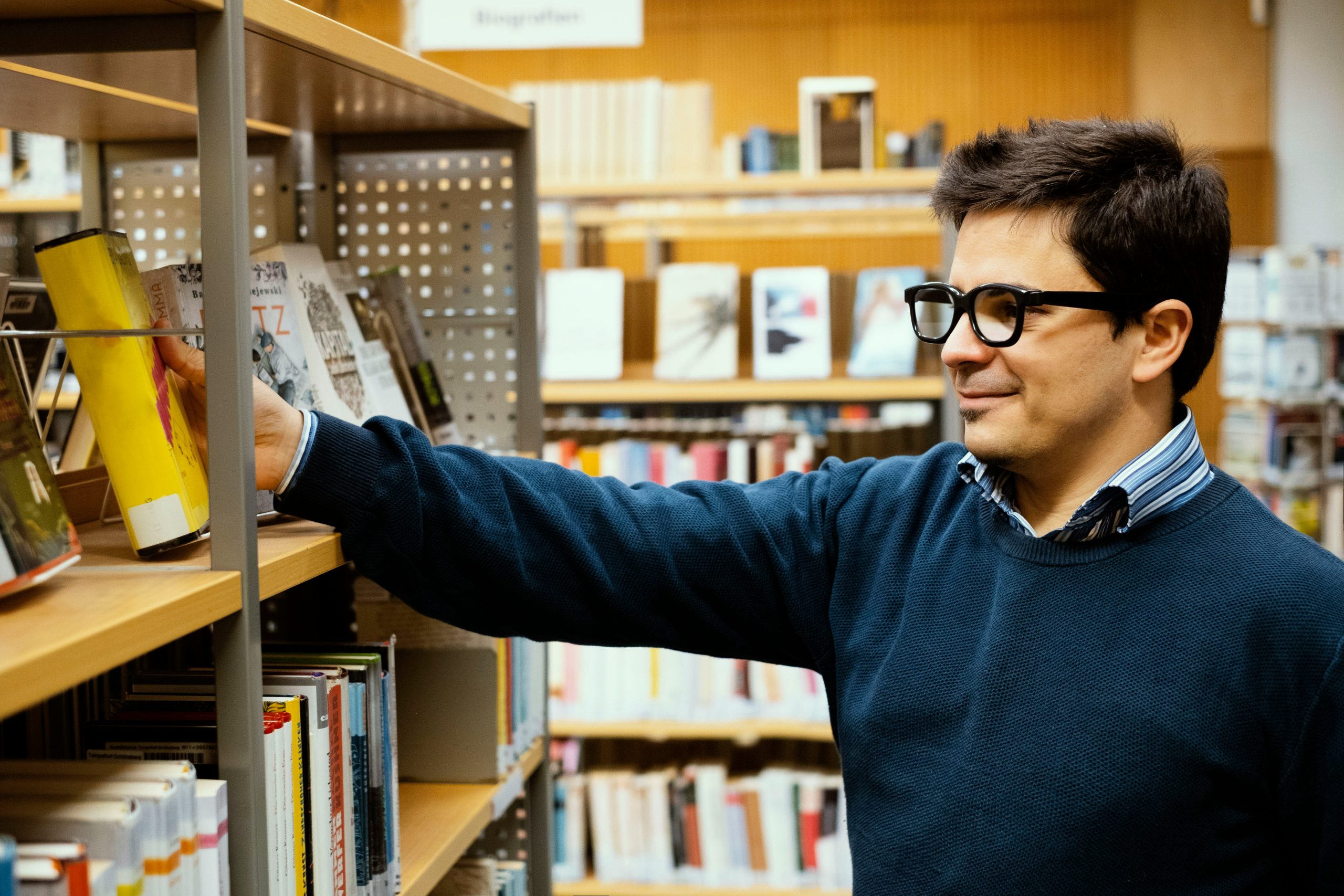 A young male librarian arranging a book on a shelf.