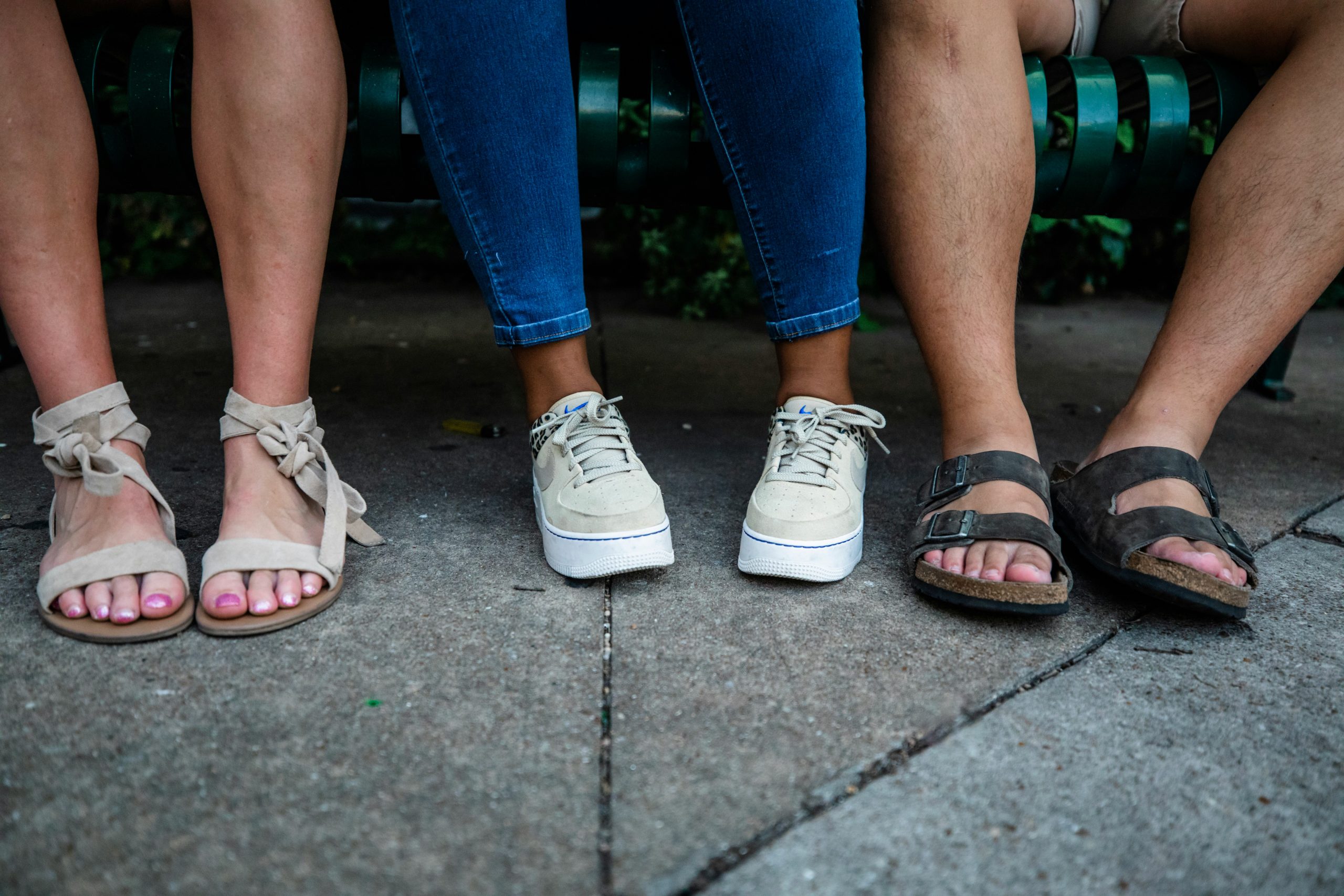 A close-up of three people's feet wearing sandals and running shoes.