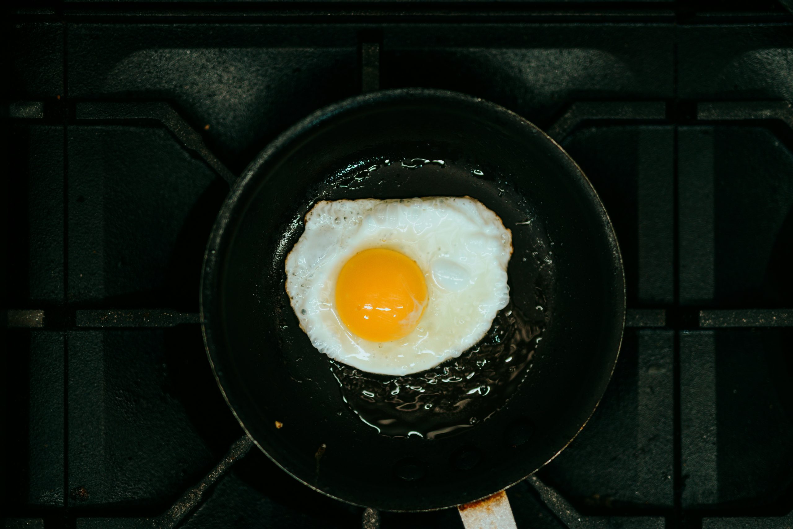 A fried egg cooking in a frying pan with oil on a stovetop.
