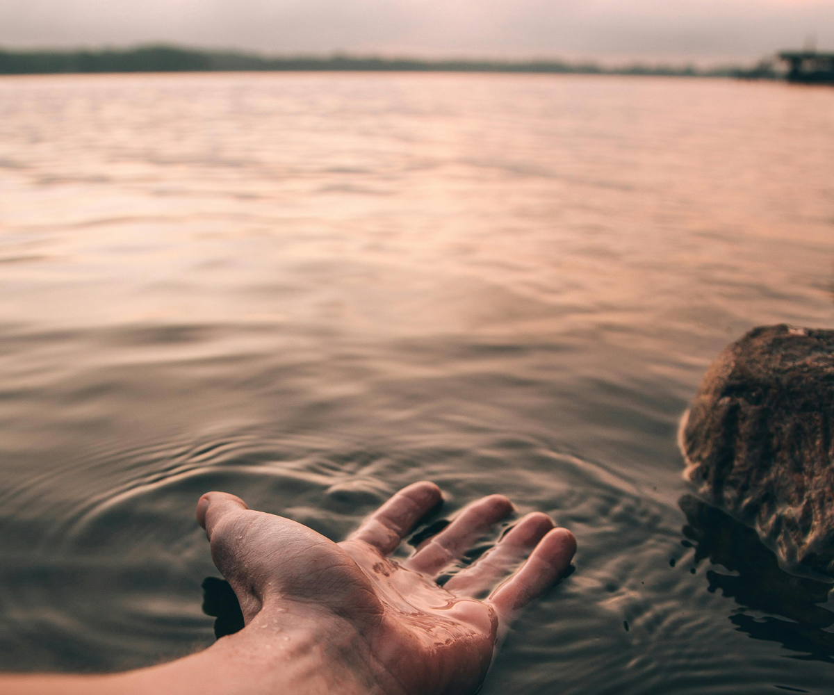 A hand stroking the water in front of a peaceful sky.