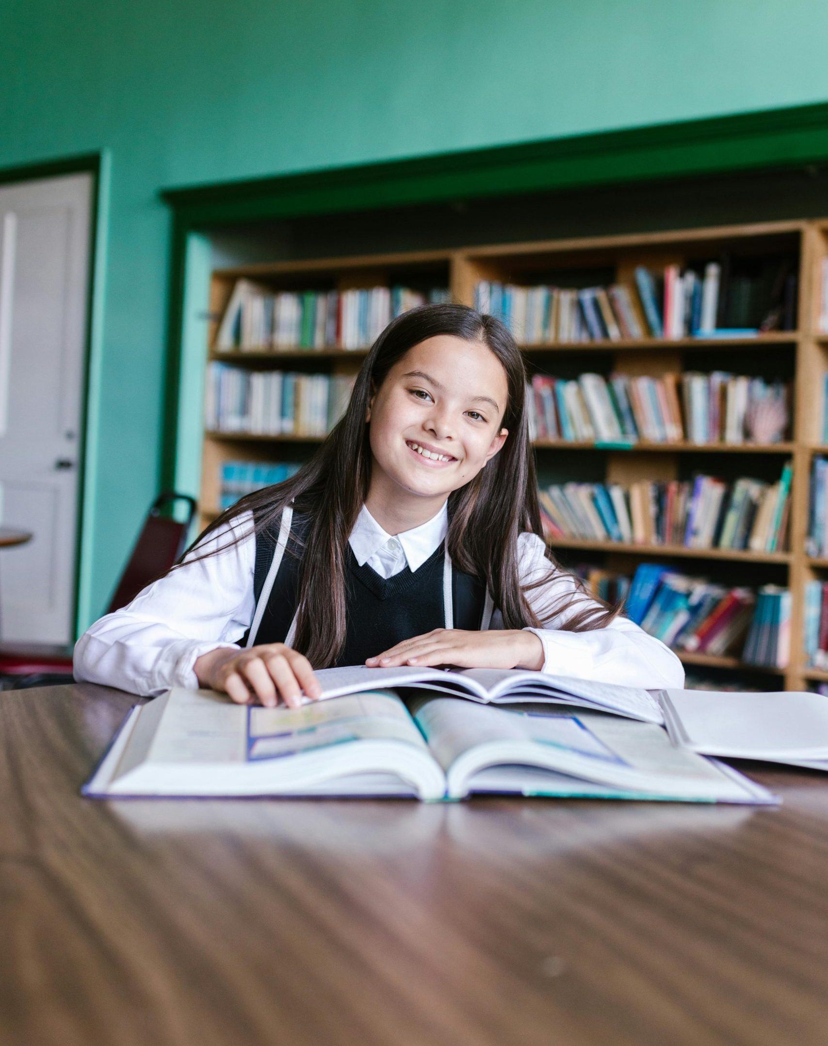 A young girl sitting at a desk with books in a school library.