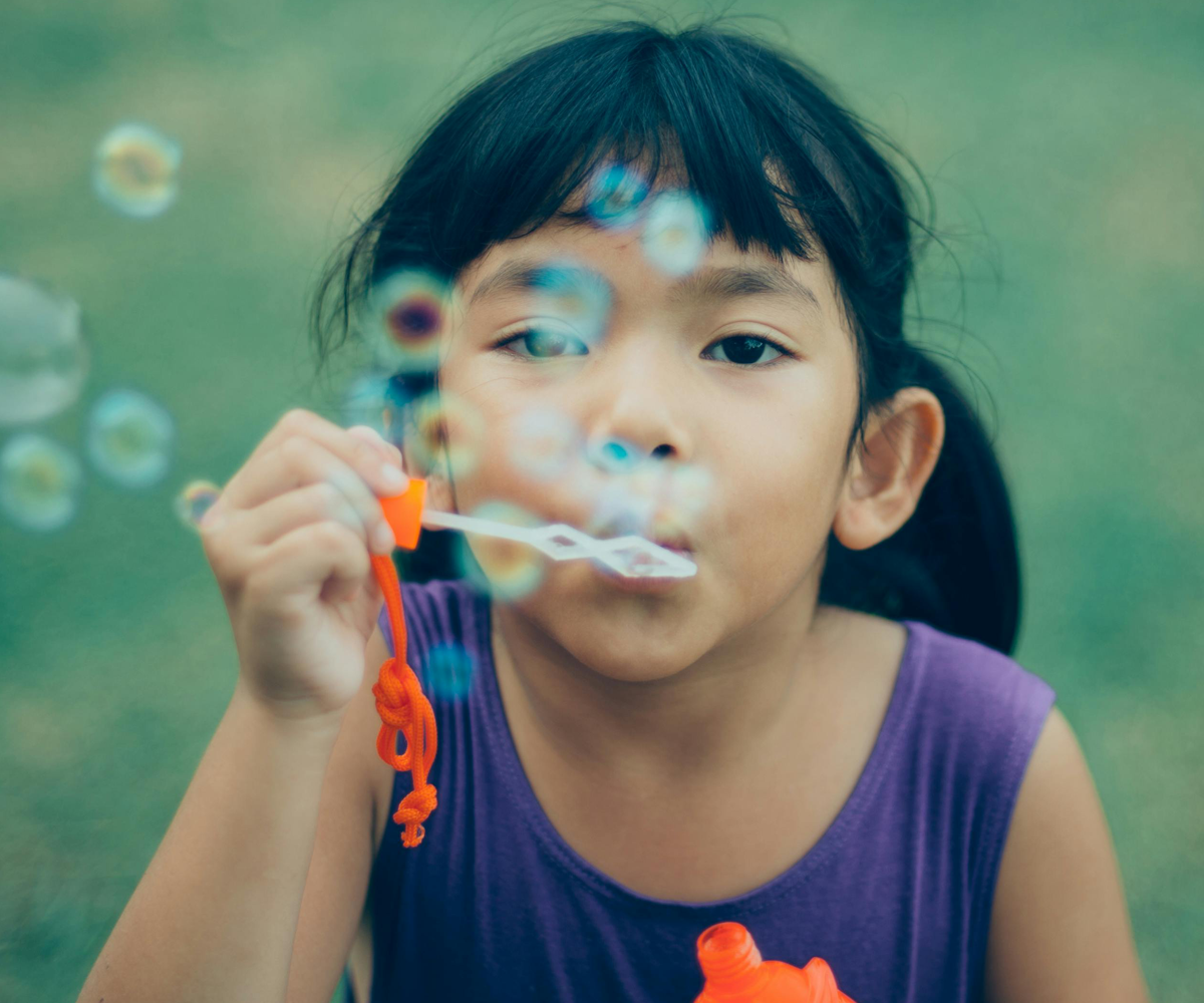 A little girl blowing bubbles outside.